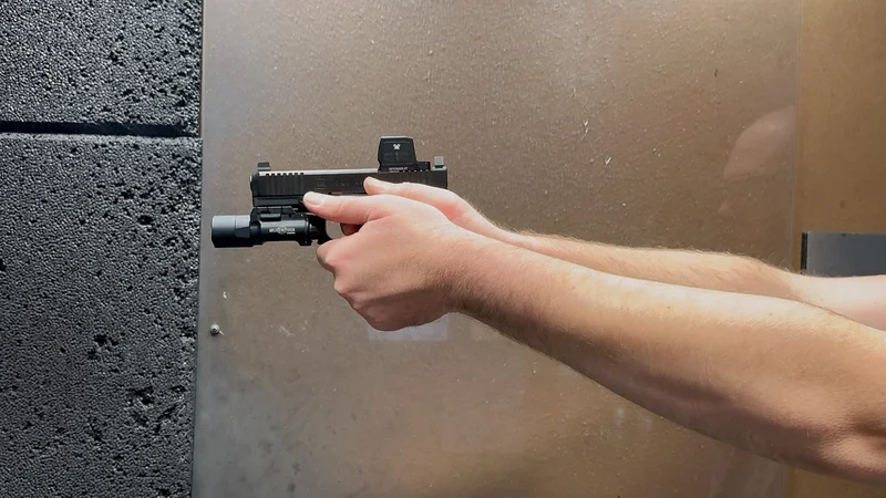 A person holding and firing a handgun equipped with the Vortex Defender-ST Enclosed Solar optic at an indoor shooting range