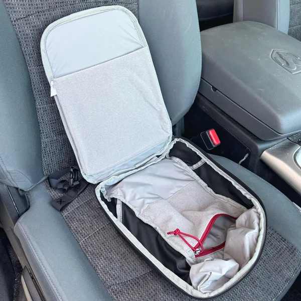 Open main compartment of sling bag on car seat, showing space suitable for a tablet or body armor panel