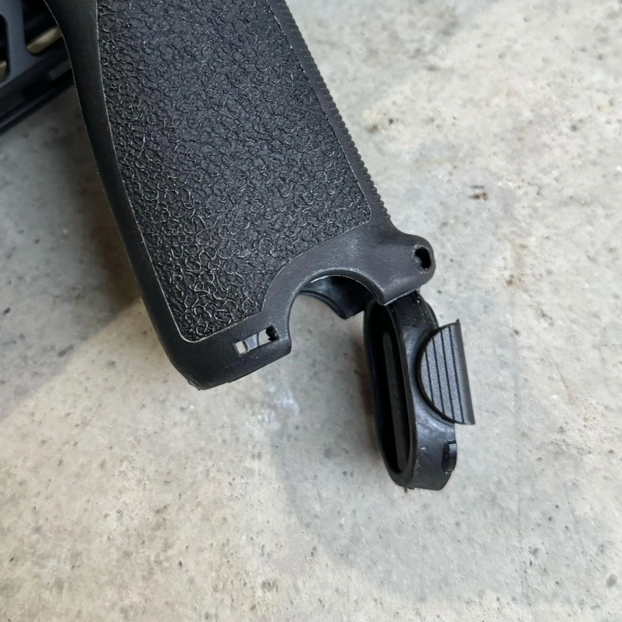 An image showing someone struggling to open the grip latch of an AR-15 grip while wearing gloves, pointing out a usability issue