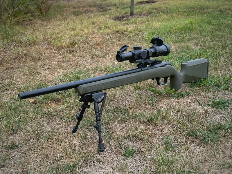 A close-up of the Springfield Model 2020 Rimfire rifle, featuring an OD green synthetic stock with black webbing. The rifle’s finish reflects a blend of durability and aesthetic appeal